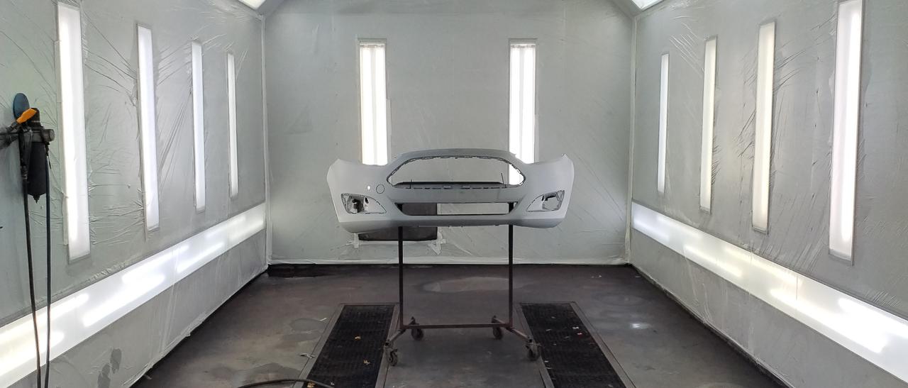 Auton etupuskuri maalattavana maalauskammiossa, puskuri asennettuna maalaustelineelle.