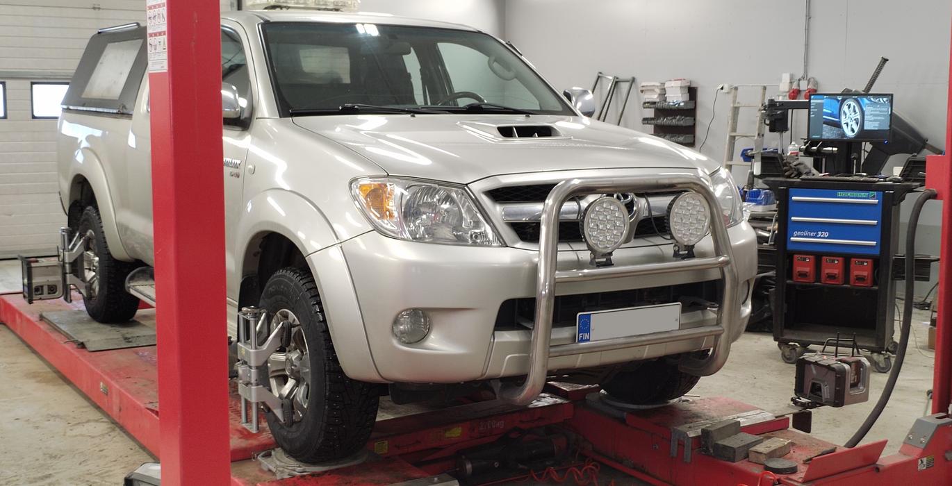 Maasturi nelipyöräsuuntauksen tarkistuksessa autokorjaamolla, jossa käytetään suuntauslaitteita.