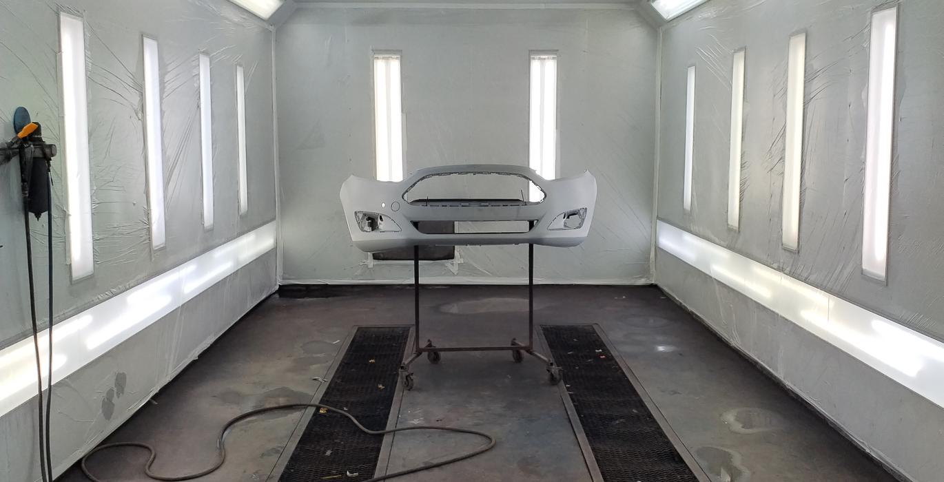 Auton etupuskuri maalattavana maalauskammiossa, puskuri asennettuna maalaustelineelle.