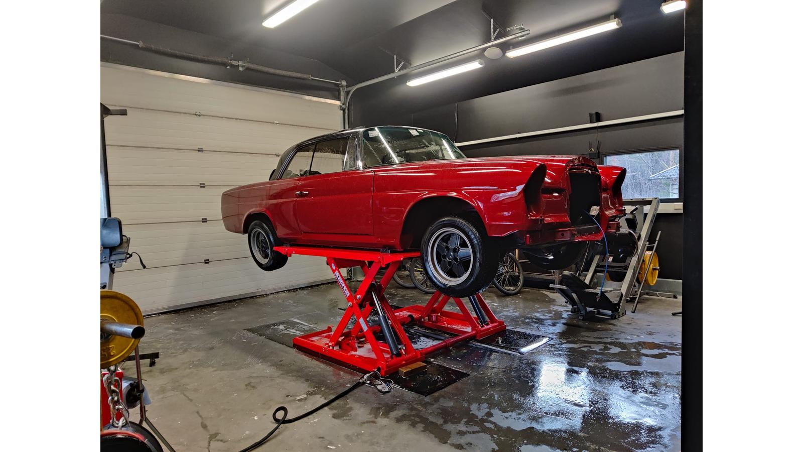 Punainen klassikkoauto nosturilla huoltotiloissa, esimerkkinä Automaalaamo Laitisen laadukkaista maalaustöistä referenssisivulla.