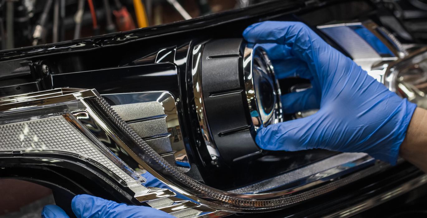 Automekaanikko kunnostamassa muovista ajovaloa sinisissä suojakäsineissä, osa huoltoprosessia.