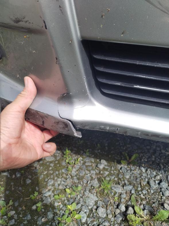 K&auml;si pitelee haljennutta auton puskuria, joka odottaa muovikorjausta.